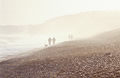 People in silhouette walking on the shingle at Dunwich, Suffolk, on the east coast of England